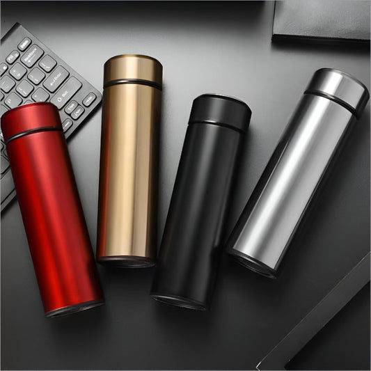 Four metallic tumblers in red, gold, black, and silver on a dark surface with a keyboard.